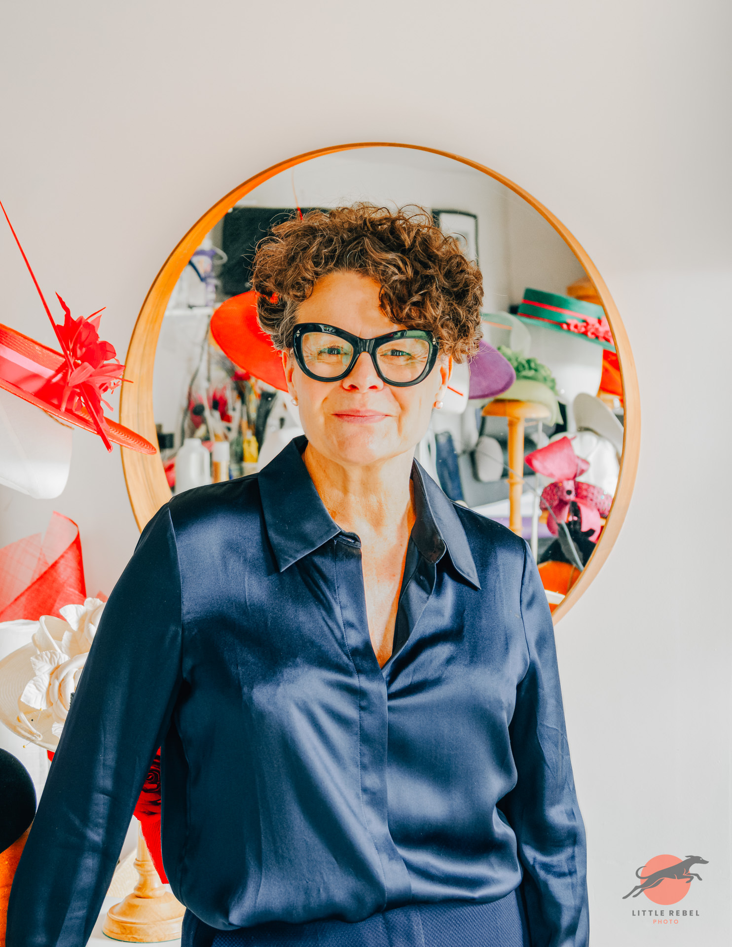 Portrait of milliner Justine Bradley-Hill in her studio surrounded by colourful hats