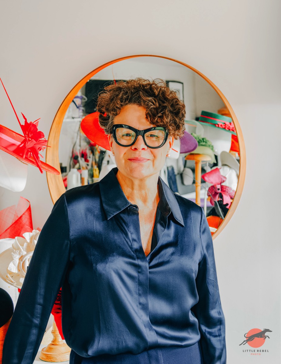Portrait of milliner Justine Bradley-Hill in her studio surrounded by colourful hats
