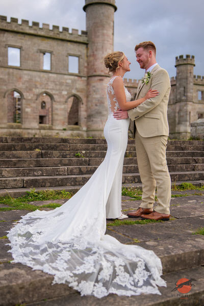Newlyweds embracing on the stone steps outside Lowther Castle in Cumbria