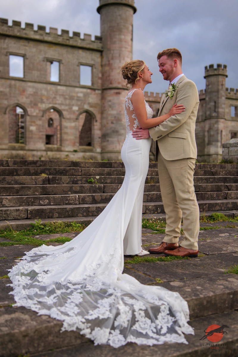 Newlyweds embracing on the stone steps outside Lowther Castle in Cumbria