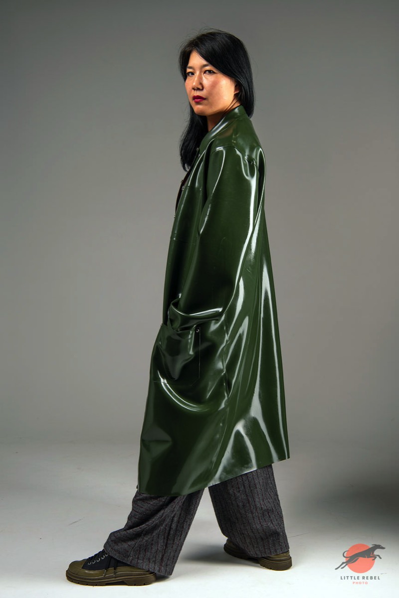 Female model wearing a glossy olive-green rubber raincoat by Wrapped in Rubber