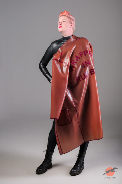 Model wearing a translucent rose-pink rubber coat with plum lettering by Wrapped in Rubber