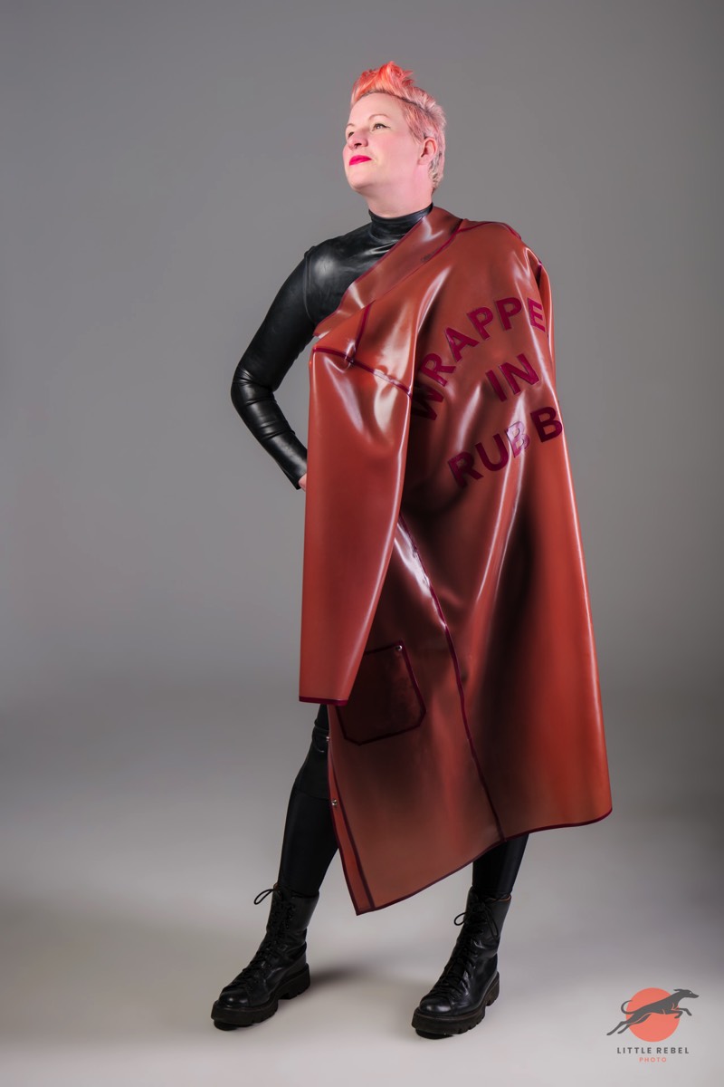 Model wearing a translucent rose-pink rubber coat with plum lettering by Wrapped in Rubber